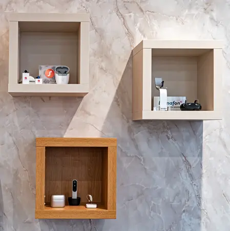 Moderne Hörgeräte und Zubehör in Wandregalen auf Marmorwand im Hörakustik-Fachgeschäft.